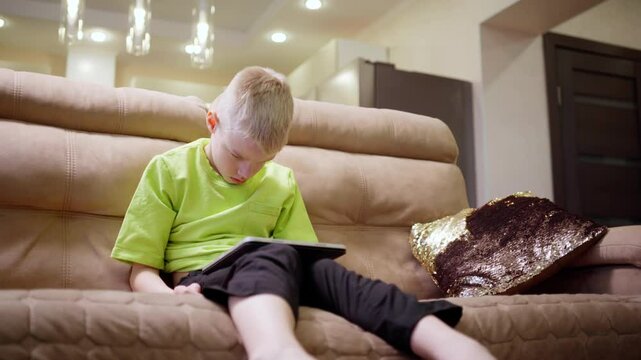 A boy with hearing aids engages with a laptop and tablet, showcasing modern childhood's digital learning and inclusive tech play. Perfect for education and disability awareness content