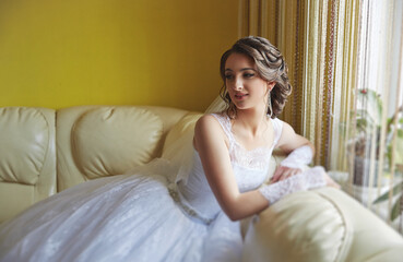 A woman in a white wedding dress is sitting on a couch