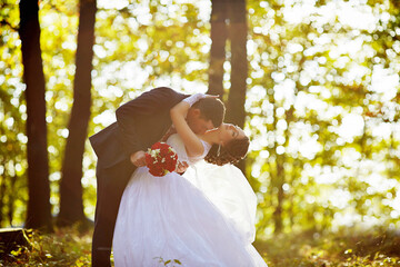 A bride and groom are kissing in the woods