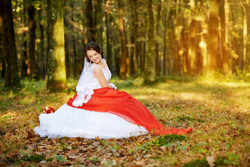 A woman in a red dress is sitting in a forest