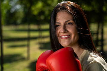 Smiling beautiful woman in boxing gloves, front view, sunny outdoor scene