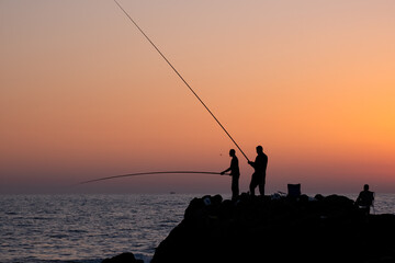 fishermen fishing in the evening by the sea on the Mediterranean sea coast of Caesarea in Israel at sunset time in the direction of the setting sun. High quality photo