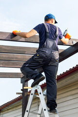  builder man with electric screwdriver installing impregnated wooden board. man  builds a wooden...