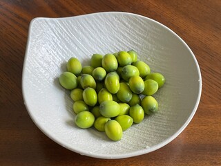 A white ceramic bowl filled with fresh green lotus seeds sits on a wooden table, showcasing smooth, round texture and vibrant hue under soft light, creating a simple yet vibrant still - life scene.