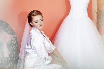 A bride is sitting in front of a white dress, getting ready for her wedding
