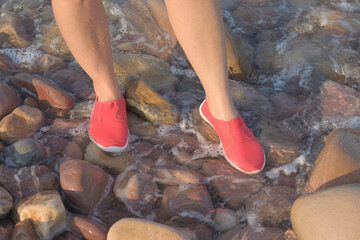 Woman wearing water shoes on a pebbly beach, booties, flip-flops, and water socks