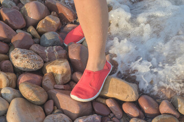 Woman wearing water shoes on a pebbly beach, booties, flip-flops, and water socks