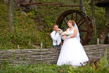 A bride and groom are standing next to a wooden fence