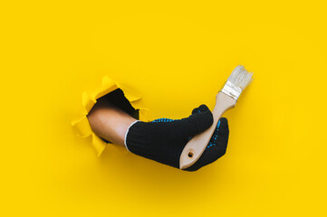 The right painter's hand in a black cloth knitted glove holds a bristle brush. Torn hole in yellow...