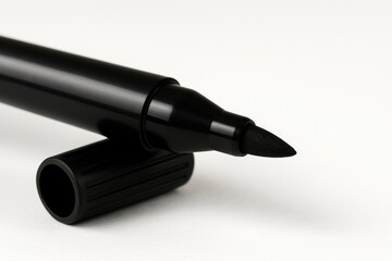 Close-up of a black felt tip pen atop its cap against a plain white backdrop