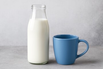 A blue mug and a glass bottle of milk placed on a gray concrete surface with ample space around