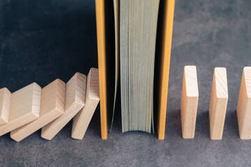 Book blocking falling dominoes, symbolizing knowledge, education, learning, and information as...