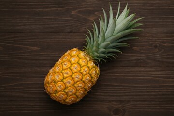 Bright yellow honey pineapple against a dark wooden surface