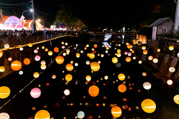 A scenic nighttime view of colorful round lanterns adorning the bridge piers above the water. The...