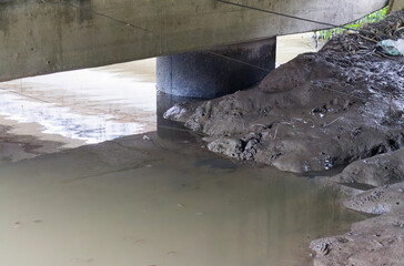 Sturdy Concrete Bridge Pier Foundation Grounded in Murky River Water with Muddy Banks and...