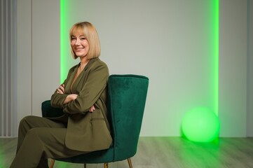 A woman in a suit sits in a green chair with arms crossed