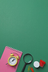 Top view of school supplies, pencils, erasers, paper clips and notebooks, on a green background....