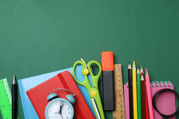 Top view of school supplies, pencils, erasers, paper clips and notebooks, on a green background....