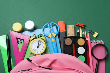 Top view of school supplies, pencils, erasers, paper clips and notebooks, on a green background....