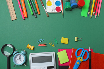Top view of school supplies, pencils, erasers, paper clips and notebooks, on a green background....