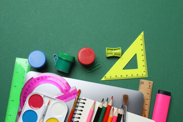 Top view of school supplies, pencils, erasers, paper clips and notebooks, on a green background....