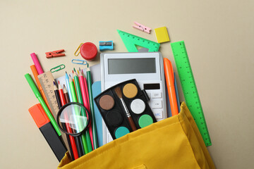 Top view of school supplies, pencils, erasers, paper clips and notebooks, on a beige background....