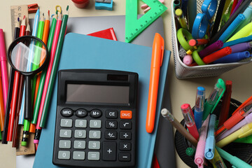 Top view of school supplies, pencils, erasers, paper clips and notebooks, on a beige background....