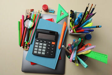 Top view of school supplies, pencils, erasers, paper clips and notebooks, on a beige background....