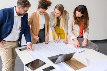 Business people examining blueprint and working on new project with computer and mobile phones on...