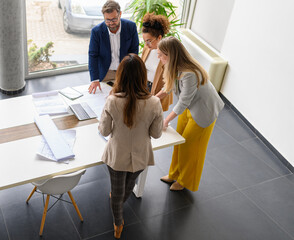High angle view of group of architects analyzing blueprint and discussing ideas while standing at...