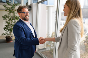 Smiling businessman in eyeglasses shaking hands with female partner after a successful business...