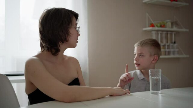 Young mother helps her hard-of-hearing son with schoolwork at home. A natural, heartfelt moment of inclusion, care, and rehabilitation, highlighting love, support, and everyday learning
