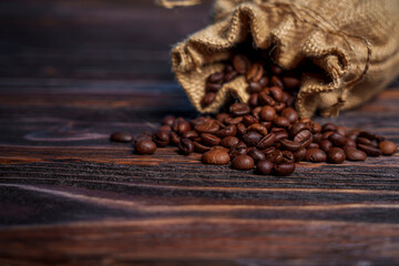 Coffee beans spilling from burlap sack onto dark wooden surface