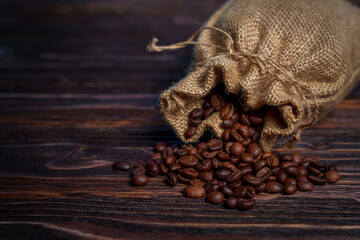 Coffee beans spilling from burlap sack onto dark wooden surface