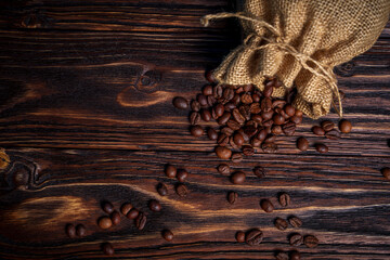 Coffee beans spilling from burlap sack onto dark wooden surface