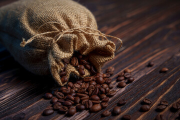 Coffee beans spilling from burlap sack onto dark wooden surface
