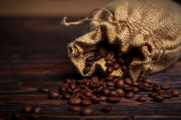 Coffee beans spilling from burlap sack onto dark wooden surface