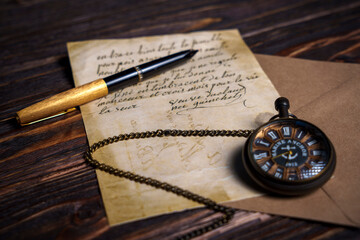 Vintage pocket watch with handwritten letter and pen on wooden surface
