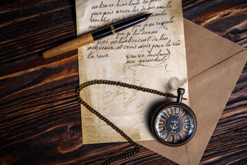 Vintage pocket watch with handwritten letter and pen on wooden surface