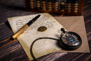 Vintage pocket watch with handwritten letter and pen on wooden surface