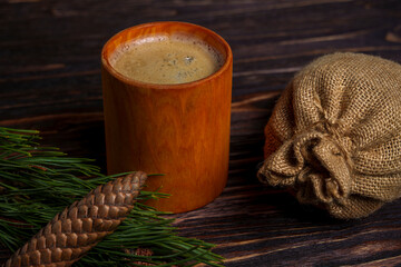 Rustic coffee cup with pine cone, burlap sack, and evergreen on wooden table