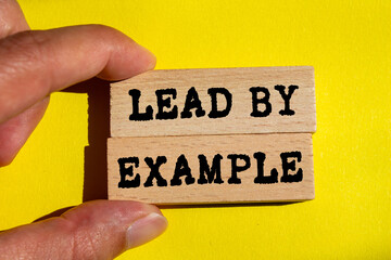 Lead by example message written on wooden blocks on yellow background. Conceptual lead by example...