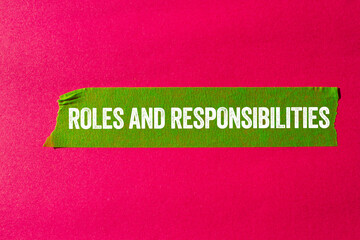 Roles and responsibilities message written on ripped torn green paper tape on pink background....