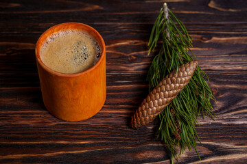 Cup of coffee with pine cone and evergreen branch on wooden table