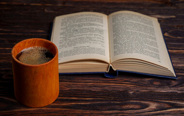 Open book and coffee cup on dark wooden table in warm light