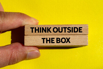 Think outside the box message written on wooden blocks on yellow background. Conceptual think...