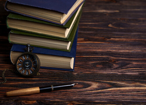 Stack of books with vintage pocket watch and fountain pen on wooden table