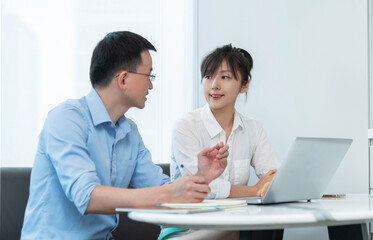 Two asian businesspeople working together in the office while using laptop