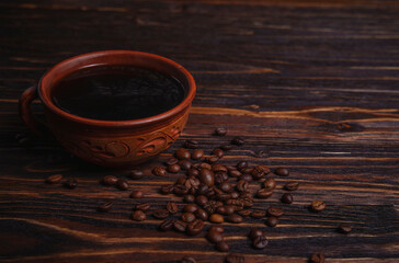 Cup of black coffee with scattered coffee beans on dark wooden table
