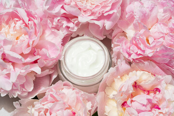 Open cream jar with pink peonies on soft backdrop. Fresh, floral beauty flat lay for skincare...